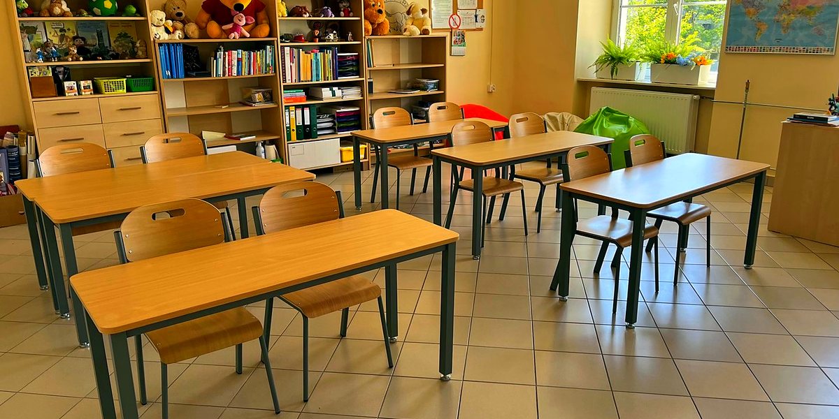 Przytulna sala edukacji wczesnoszkolnej z ławkami, regałami książek, maskotkami i mapą świata